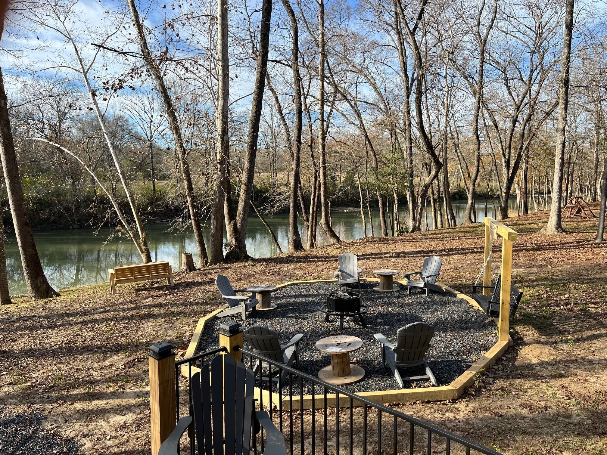Un camping junto al lago con sillas Adirondack, un hoyo para fuego y un banco.