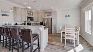 Una cocina moderna con armarios blancos, una isla central con taburetes y electrodomésticos como refrigerador y microondas.
