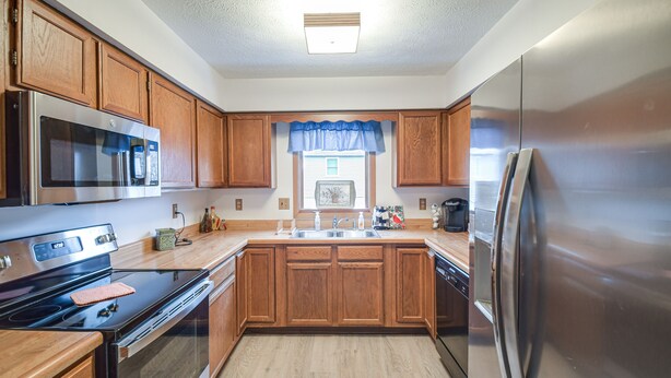 A kitchen with wooden cabinets, stainless steel appliances, a window with a blue valance, and a built-in oven. - Welcoming Condo in Davenport: Central Location! (Davenport)