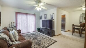 A living room with a brown sofa, a large rug, a ceiling fan, and a flat-screen TV on a stand. - Welcoming Condo in Davenport: Central Location! (Davenport)