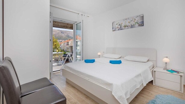 A bedroom with a bed, bedside table, and a view of the outside.