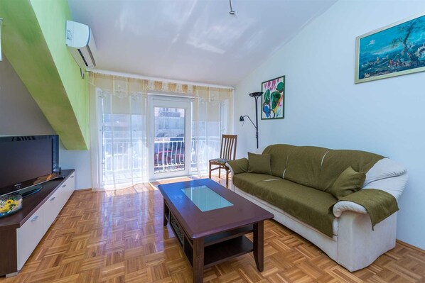 A living room with a sofa, a TV, a table, and a balcony.