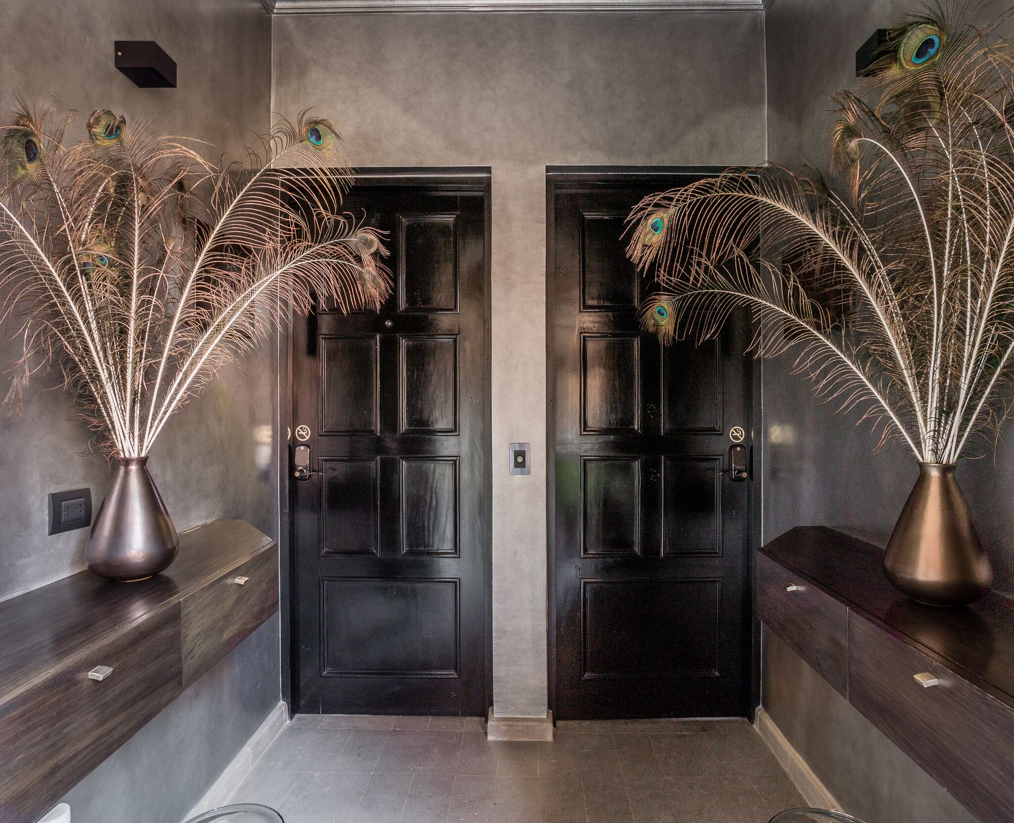 A hallway with two black doors, each adorned with a decorative peacock feather arrangement in a vase.