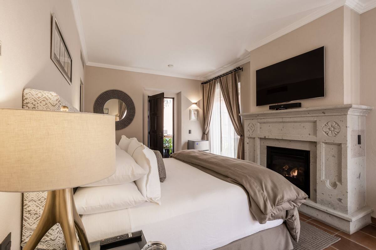 A bedroom with a bed, a television, a fireplace, and a view of the outside.