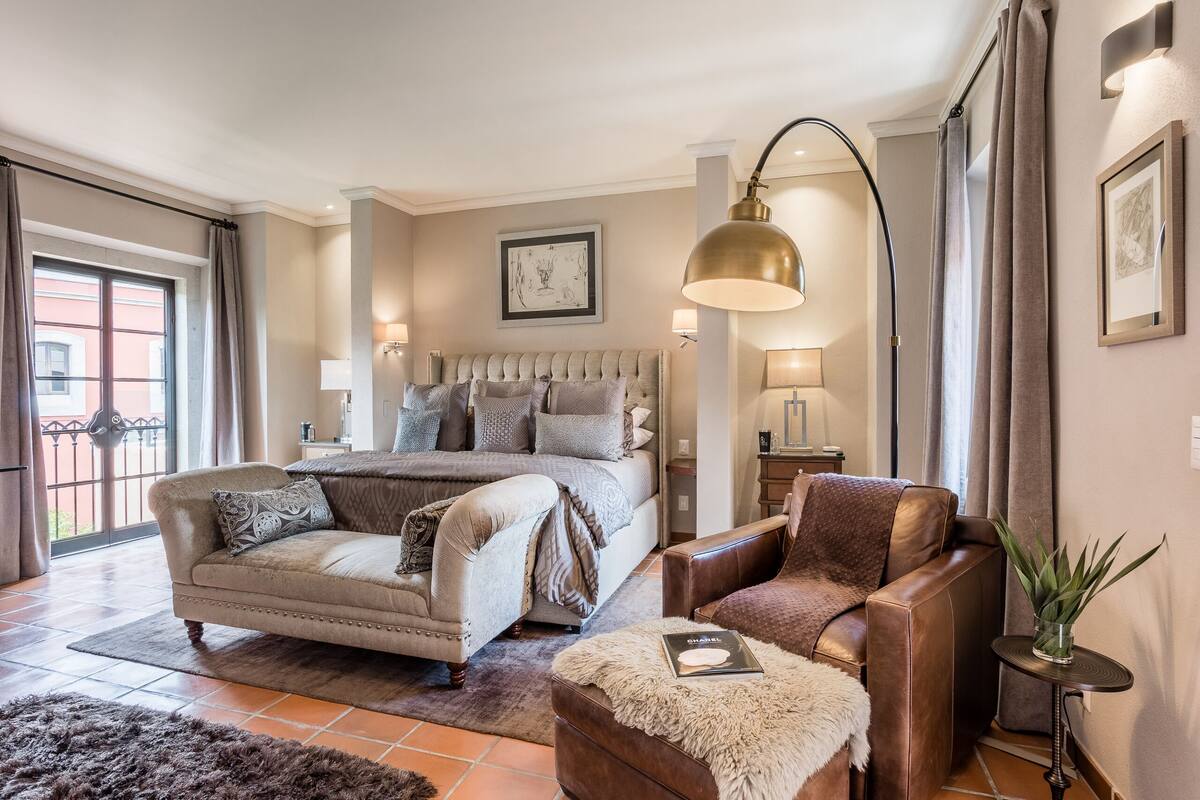 A bedroom with a large bed, a sofa, a small table with a plant, and a lamp.