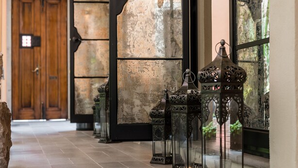 A hallway with ornate lanterns, a wooden door, and a stone wall. - Artesana – Privately Owned Rosewood Residence (San Miguel de Allende)