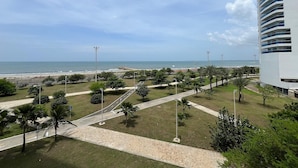 A coastal view with a paved walkway, palm trees, and a modern building with balconies overlooking the beach.