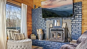 A cozy living room with a stone fireplace, a comfortable seating area, and a large window with curtains. - Epic Views| 3 Pools!| Dog Friendly| Gatlinburg, GSMNP 10 Minutes (Gatlinburg)