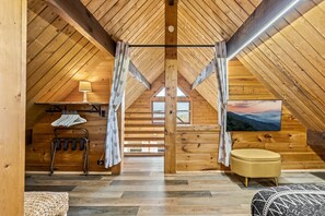A cozy attic bedroom with wooden walls, a ceiling fan, a TV, and a window with a view.