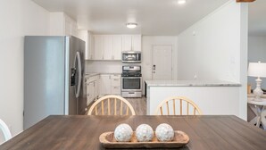 Une cuisine moderne avec des meubles blancs, des appareils en acier inoxydable et une table à manger en bois sur laquelle est posé un plateau contenant des œufs décoratifs.