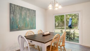 Un coin repas avec une table en bois, des chaises blanches et un grand tableau abstrait accroché au mur.