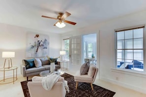 Un salon moderne avec un canapé gris, un fauteuil beige, une table basse et un ventilateur de plafond.