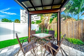 An outdoor patio with a glass-top table and wicker chairs, surrounded by a bamboo fence and tropical plants. - Heated Pool+Hot Tub! Walk To Beach & Shops! (Fort Lauderdale)