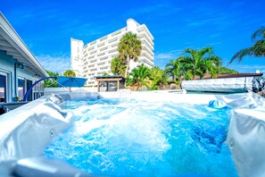 Une piscine d’hôtel entourée de palmiers, avec un jacuzzi et un bâtiment visible au loin.