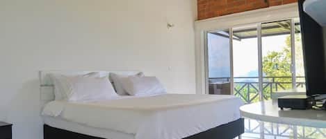 Un dormitorio con una cama grande, ropa de cama blanca, una pared de ladrillo y un balcón con mesa y silla.