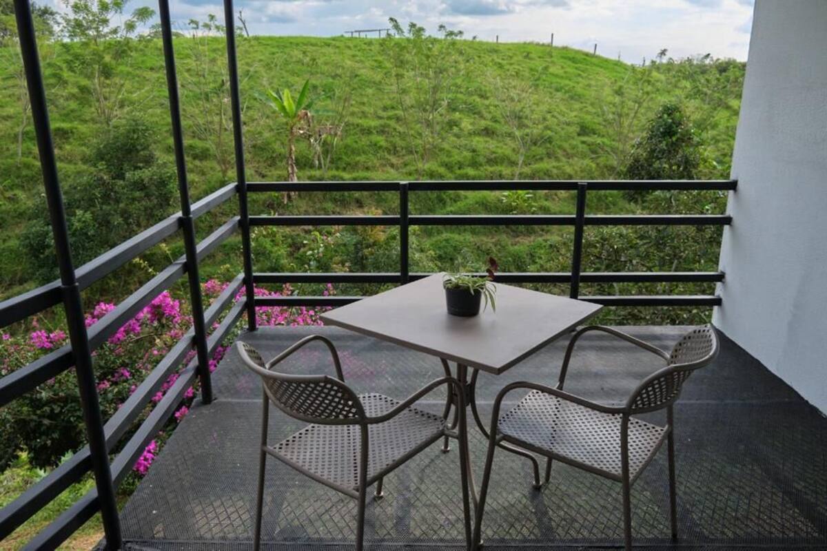 A balcony with a table and two chairs, overlooking a lush green hillside.