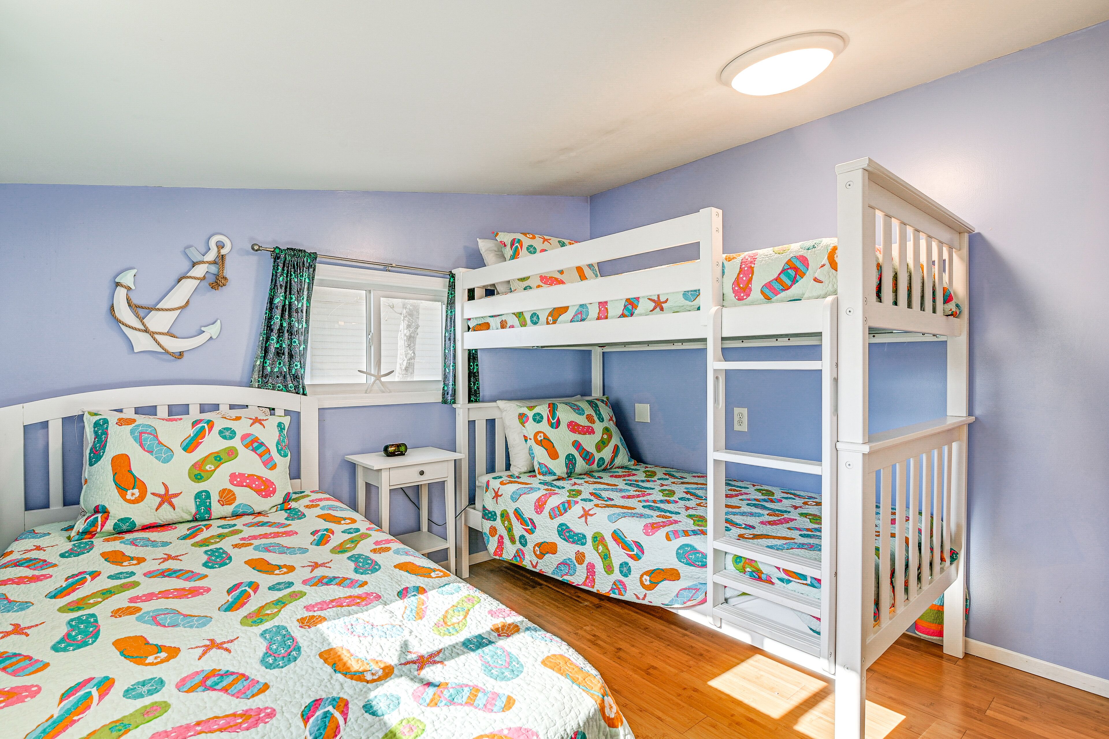 Une chambre d’enfant avec des lits superposés, une petite table de chevet et une fenêtre avec des rideaux.