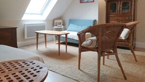 Una habitación acogedora con techo inclinado, un armario de madera, una silla de mimbre, una mesita pequeña y un sofá azul.