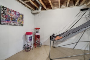 A room with a white wall, a colorful poster, a red and white cart, and a metal ladder. - FamilyNest/King Bd/GameRoom (Royal Oak)
