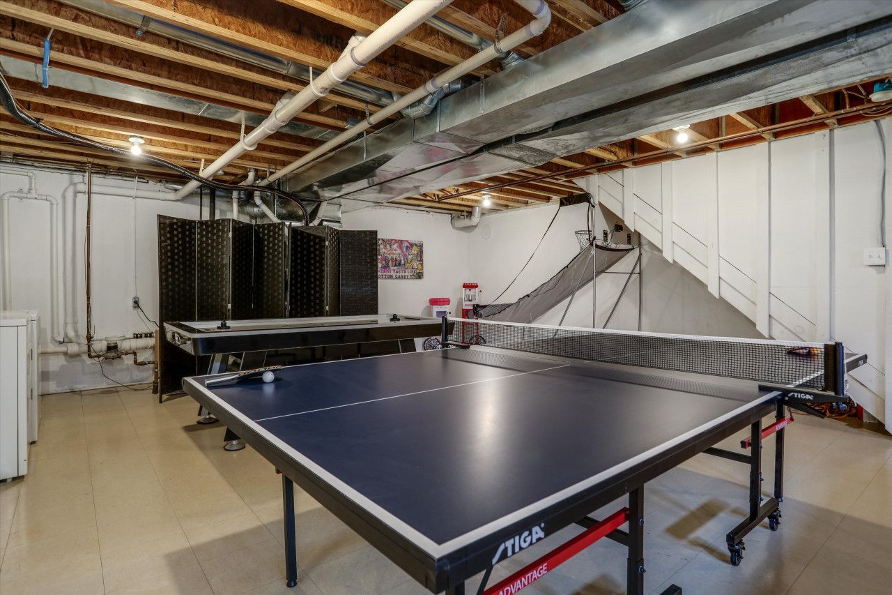 Una mesa de ping pong en una habitación con vigas de madera a la vista y tuberías visibles.