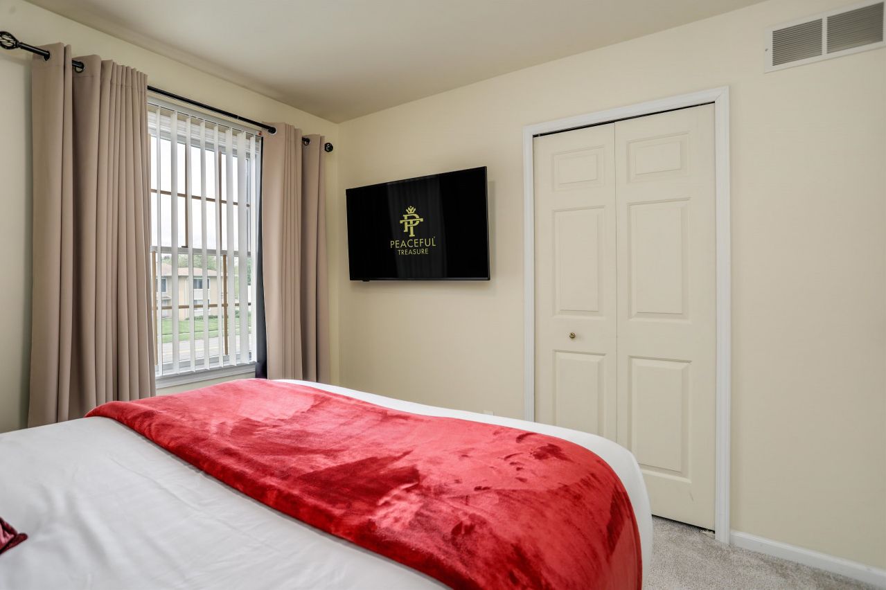 A hotel room with a bed, a TV on the wall, a door, and a window with curtains.
