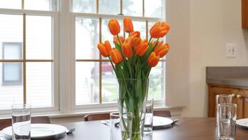 Ein Esstisch mit einer Vase orangener Tulpen, klaren Gläsern und Tellern, die für eine Mahlzeit gedeckt sind.