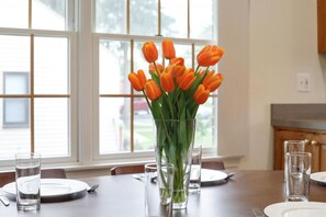A dining table with a vase of orange tulips, clear glasses, and plates set for a meal.