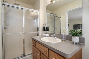 A bathroom with a glass-enclosed shower, a sink with a mirror above it, and wooden cabinets. - FamilyNest/King Bd/GameRoom (Royal Oak)