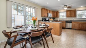 A modern kitchen with wooden cabinets, a central island, and a dining area with chairs and a table set for four. - FamilyNest/King Bd/GameRoom (Royal Oak)