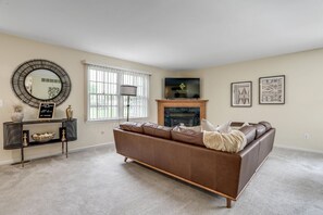 A living room with a brown leather sofa, a fireplace, a television, and framed artwork on the wall.