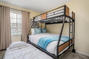 A bunk bed room with a window, curtains, and a bed with a blue blanket.
