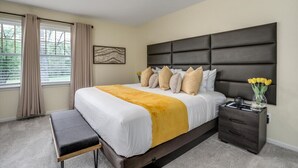 A bedroom with a large bed, a bedside table, a bench, and a window with curtains. - FamilyNest/King Bd/GameRoom (Royal Oak)