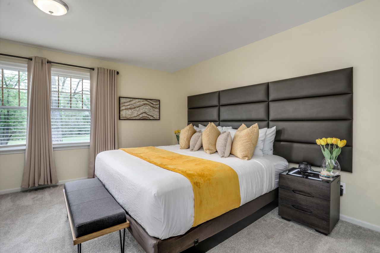 A bedroom with a large bed, a bedside table, a bench, and a window with curtains.
