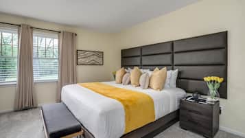 A bedroom with a large bed, a bedside table, a bench, and a window with curtains.