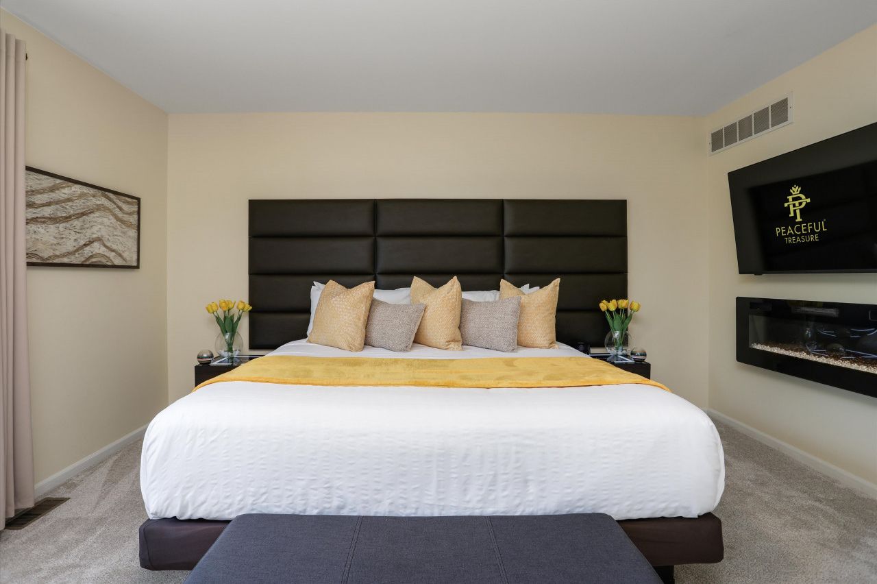 Une chambre d’hôtel moderne avec un grand lit, une tête de lit sombre et un téléviseur à écran plat fixé au mur.