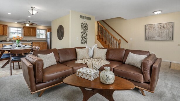 A living room with a brown leather sectional sofa, a coffee table, and a dining area with wooden cabinets and a chandelier. - FamilyNest/King Bd/GameRoom (Royal Oak)