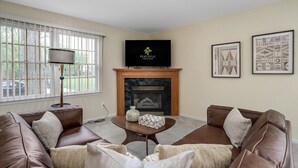 A living room with a fireplace, a television, and framed artwork on the wall. - FamilyNest/King Bd/GameRoom (Royal Oak)