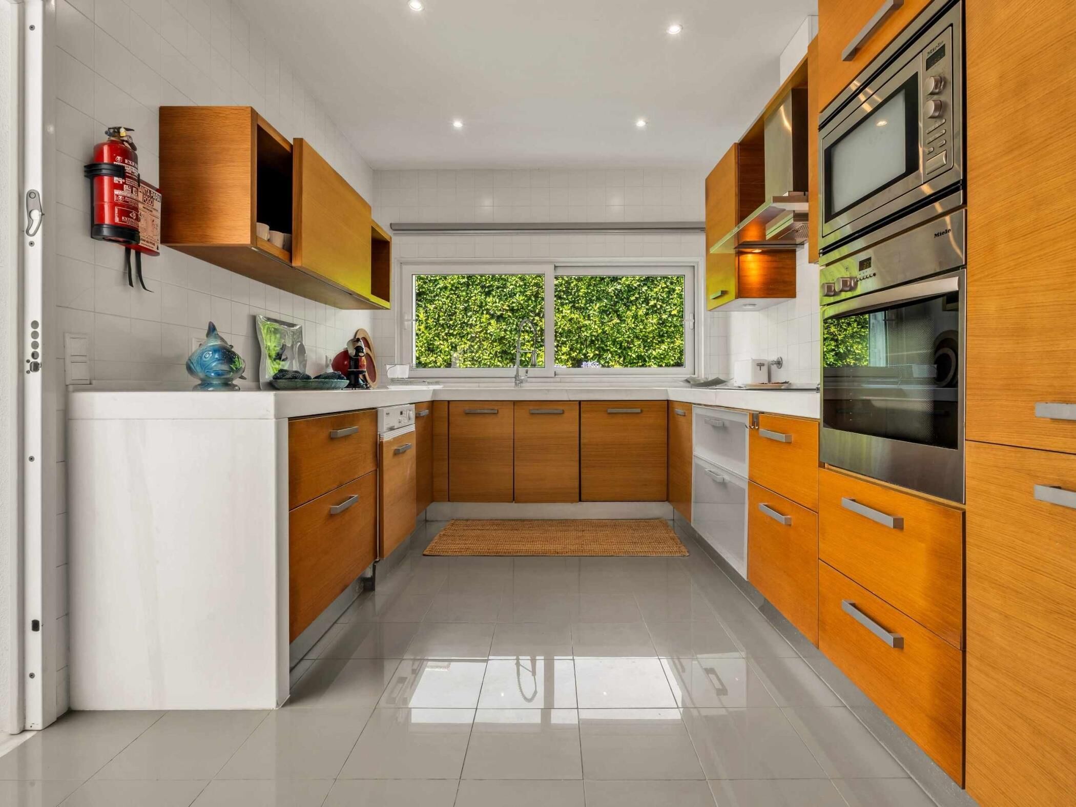 Una cucina moderna con mobili in legno, elettrodomestici in acciaio inossidabile e una finestra con vista su un ambiente verde.