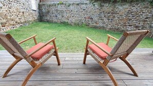 Two wicker chairs with red cushions on a wooden deck.