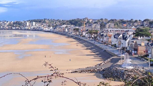 A coastal town with a sandy beach, stone walls, and buildings along the shore.