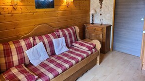 A wooden cabin interior with a sofa, two wall-mounted lamps, a framed picture, and a small wooden cabinet. - Studio 4/6pers, Terrasse, Jardinet, vue Imprenable sur la Muselle.50m des Pistes (Les Deux Alpes)