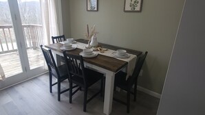 Ein Essbereich mit Tisch für vier Personen, Stühlen, einer Vase mit Trockenpflanzen und zwei gerahmten Bildern an der Wand.