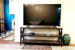A TV on a wooden stand with shelves, a green vase, and a patterned rug.