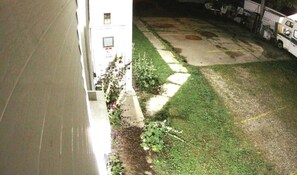 A courtyard with a white building, a paved area, and a parked vehicle.