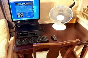A wooden table with a desktop computer, keyboard, mouse, and a standing fan.