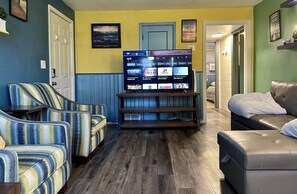 A living room with striped armchairs, a leather sofa, a TV on a wooden stand, and a door leading to another room. - Northern Lights 3pm checkout! (Moorhead)