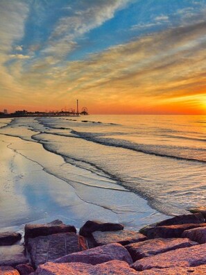 Una playa con olas, un muelle y un atardecer.