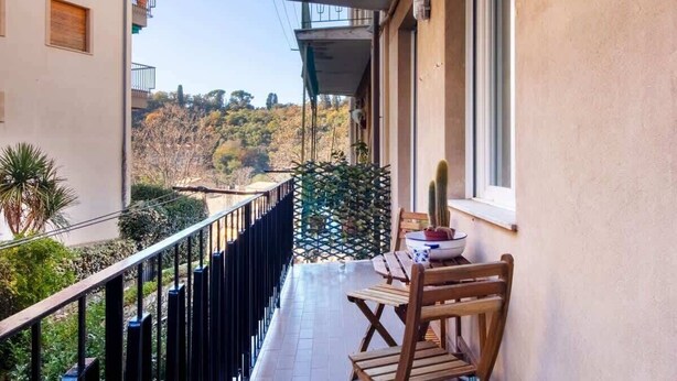 Un balcon donnant sur une colline, une table avec des chaises et un cactus.