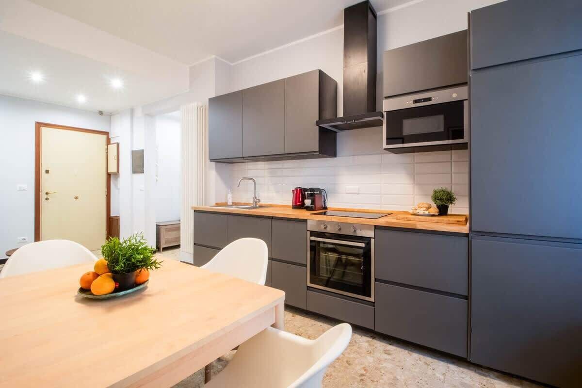 Eine moderne Küche mit grauen Schränken, einer Holz Arbeitsplatte, einem eingebauten Backofen und einer schwarzen Dunstabzugshaube.