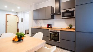 Une cuisine moderne avec des armoires grises, un plan de travail en bois, un four encastré et une hotte noire.